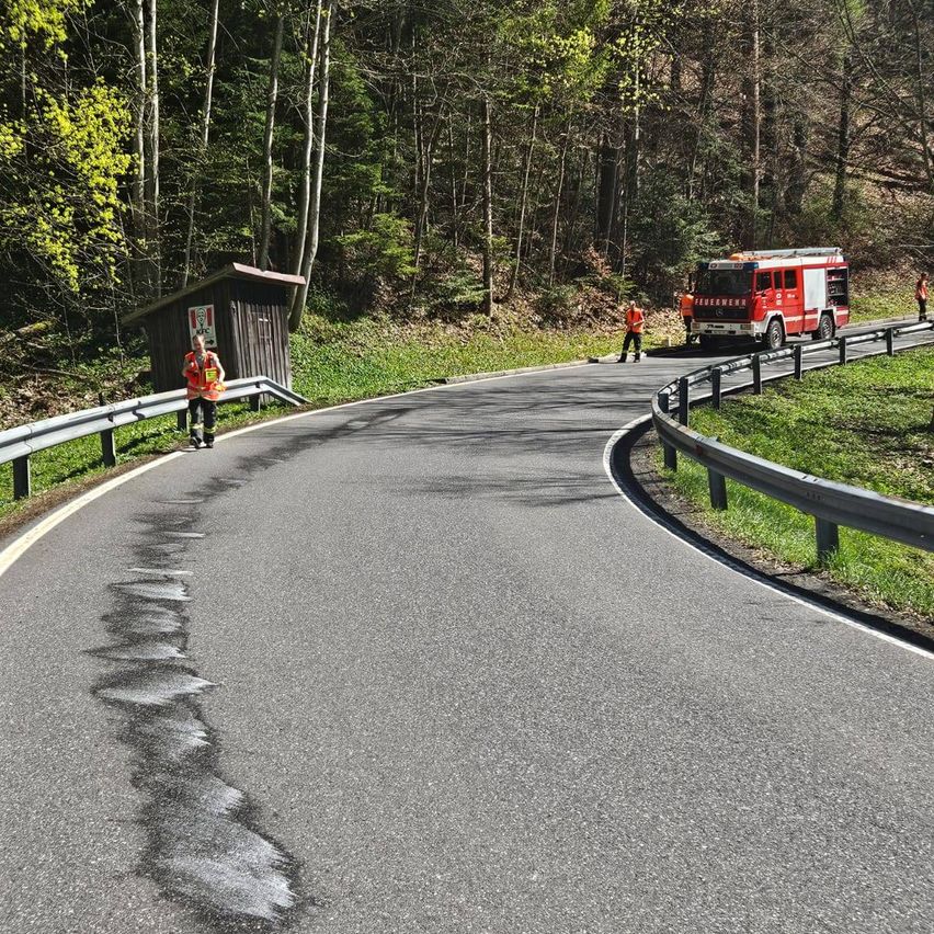 A winding road with a firefighter cleaning the road. A person stands near a guardhouse. A fire truck is parked on the right side.