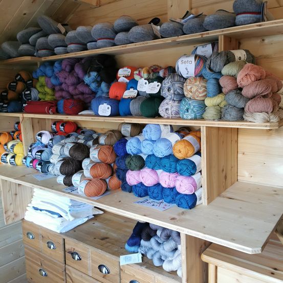Ein hölzerner Laden mit Regalen voller Wolle in verschiedenen Farben, ordentlich organisiert und ausgestellt. Jedes Wollknäuel ist mit seinem Namen beschriftet.