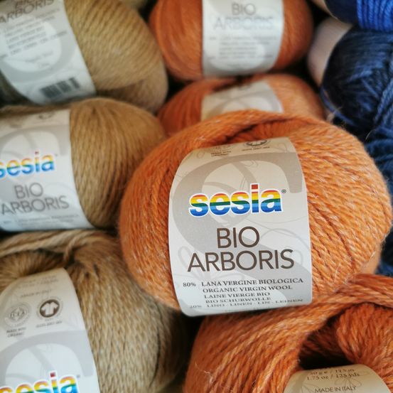 Eine Sammlung von orangefarbenen und beigen Garnen mit 'sesia BIO ARBORIS' Etiketten, übereinander gestapelt.