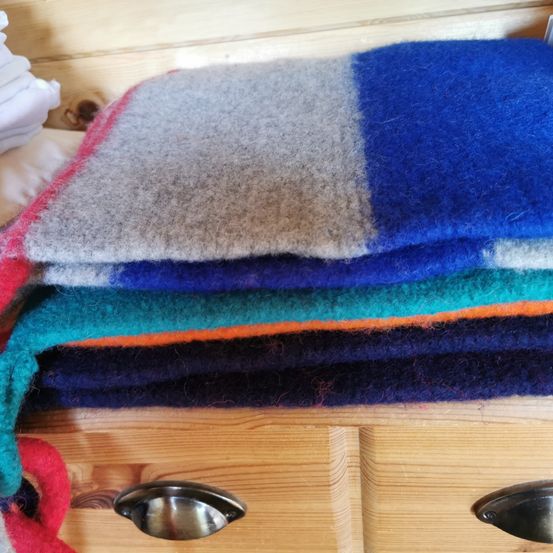 Ein Stapel farbenfroher Wolldecken auf einer hölzernen Schublade mit silbernen Griffen.