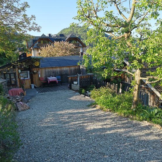 Ein Haus mit einer Kiesauffahrt und einer Terrasse mit Gartenmöbeln. Bäume und Grünflächen umgeben das Gebiet.