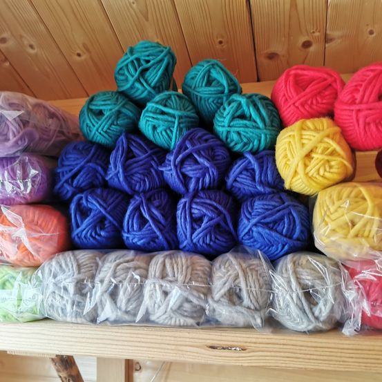 A wooden shelf displays various colored yarn balls, wrapped in plastic, against a wooden background.