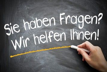 Eine Hand schreibt auf eine Tafel auf Deutsch. Es steht: 'Haben Sie Fragen? Wir helfen Ihnen!' Die Schrift ist in gelbem Marker.