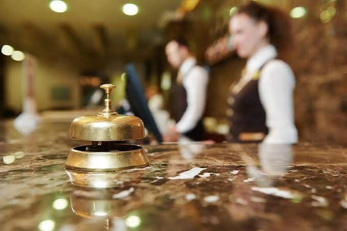 Eine goldene Glocke auf einem Marmortresen mit zwei verschwommenen Personen im Hintergrund, wahrscheinlich Hotelpersonal.