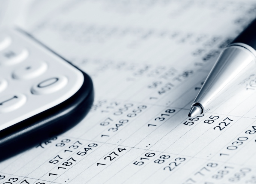 A close-up of a calculator and a pen with blurred financial numbers in the background. The calculator has a black border, and the pen is silver.