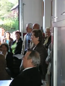 Eine Gruppe von Menschen steht in einem Raum, wahrscheinlich bei einer Versammlung. Einige schauen nach vorne, andere schauen nach links.