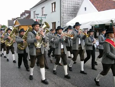 Eine Blaskapelle mit Tubas und Trompeten, die in einer Parade marschiert und traditionelle bayerische Kleidung trägt.