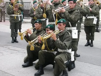 Eine Gruppe von Soldaten in grünen Uniformen spielt Trompeten und Posaunen bei einer Parade im Freien.