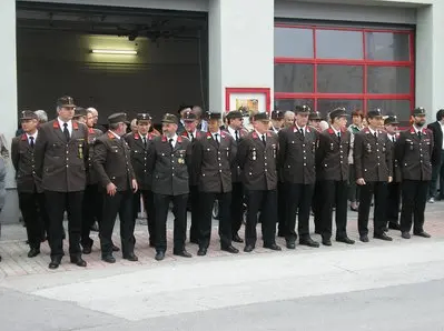 Eine Gruppe uniformierter Militärangehöriger steht in einer Reihe auf einer Straße, mit einem Gebäude im Hintergrund.