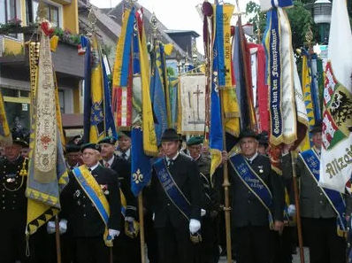Eine Gruppe von Männern in Uniformen mit Hüten und Handschuhen marschiert bei einer Parade mit vielen Flaggen und Bannern.