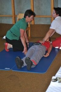 Zwei Frauen üben Erste Hilfe an einer Puppe, die auf einer blauen Matte auf dem Boden liegt.