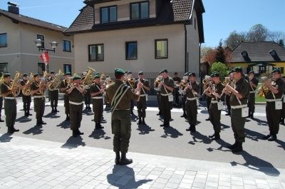 Eine Marschkapelle in Militäruniformen tritt vor einem Gebäude an einem sonnigen Tag auf.