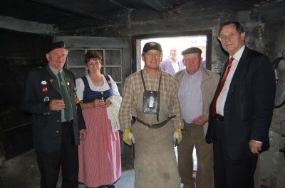 Fünf Personen stehen in einem schwach beleuchteten Raum mit einer offenen Tür. Sie sind alle formell gekleidet. Der Mann auf der rechten Seite trägt eine Krawatte.