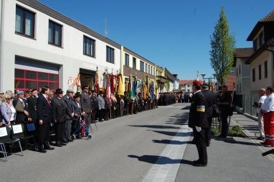 Eine Reihe von Menschen in formeller Kleidung steht in der Mitte der Straße, mit Fahnen und Gebäuden an der Seite.
