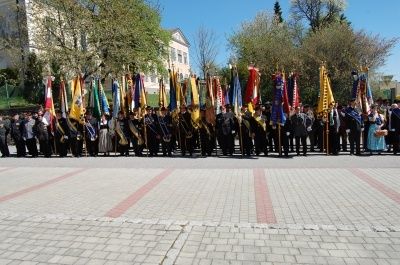 Eine Gruppe von Menschen in formeller Kleidung steht in einer Reihe und hält Flaggen. Die Flaggen sind in verschiedenen Farben, und die Menschen tragen Hüte und Handschuhe.