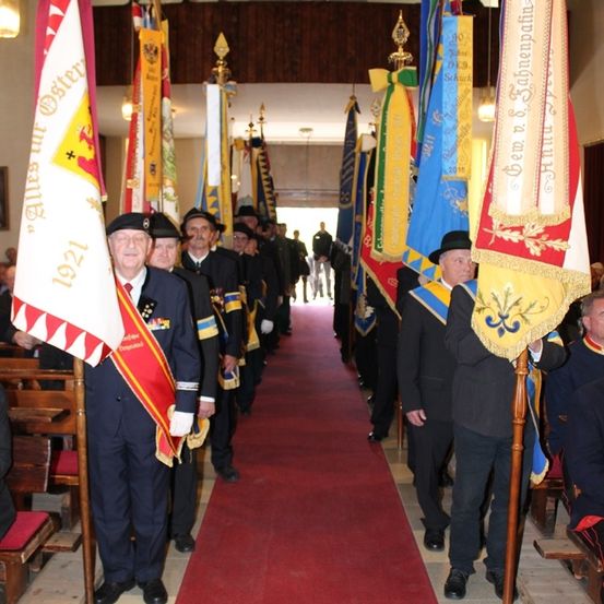 Männer in Uniformen gehen auf einem roten Teppich mit Fahnen auf beiden Seiten in einer Kirche.