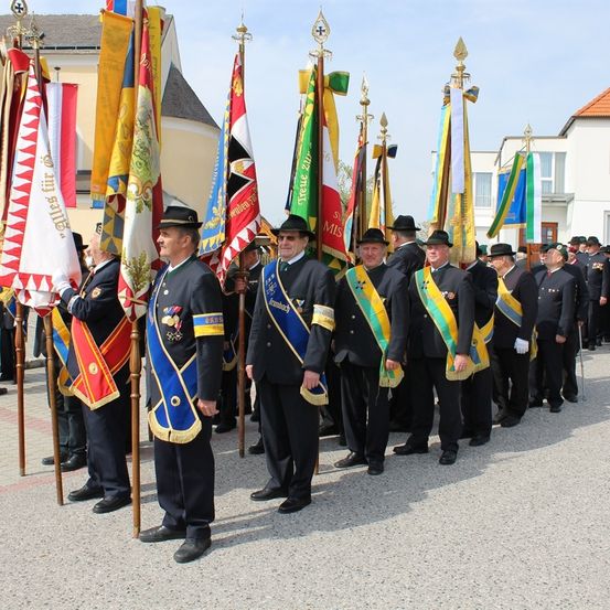 Eine Gruppe von Männern in Uniform mit Medaillen und Flaggen steht in einer Reihe auf einer Straße.