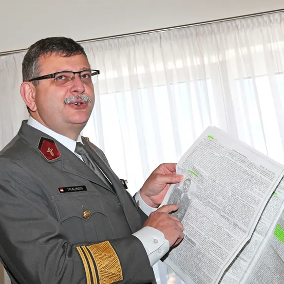 Ein Mann in Uniform hält ein Dokument mit Text vor einem Fenster.