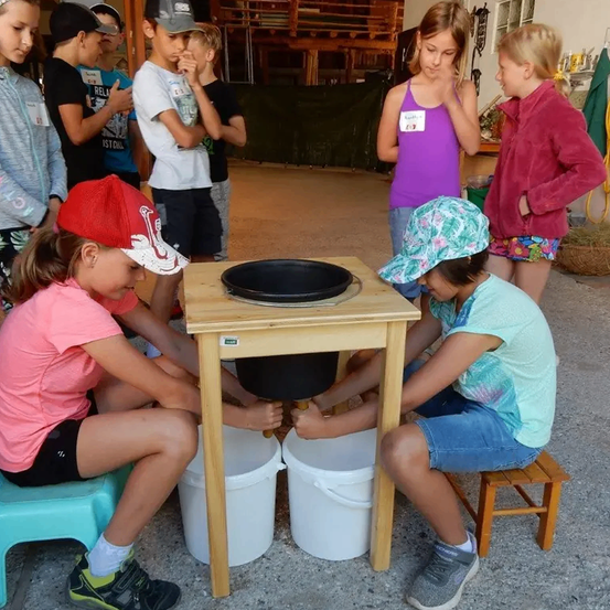 Kinder sitzen auf Stühlen und halten einen Eimer unter einem Holztisch mit einer schwarzen Schüssel obenauf.