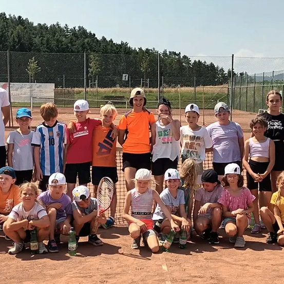 Eine Gruppe von Kindern und Jugendlichen posiert für ein Foto auf einem Tennisplatz. Einige halten Tennisschläger in den Händen.
