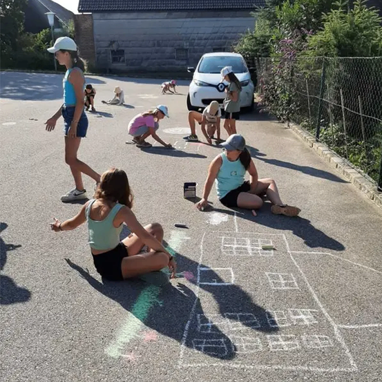 Eine Gruppe von Kindern malt mit Kreide auf der Straße. Ein Auto ist am Straßenrand geparkt.