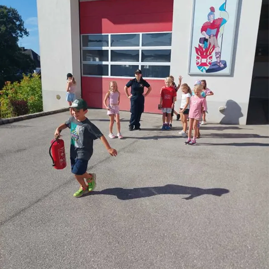 Eine Gruppe von Kindern läuft mit einem Feuerwehrmann vor einem Feuerwehrhaus.