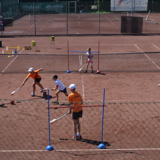 Eine Gruppe von Menschen spielt ein Spiel mit Schlägern und Bällen auf einem Tennisplatz.
