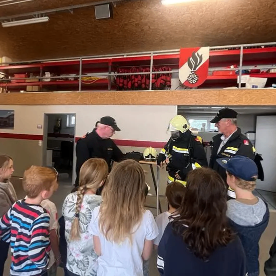 Zwei Feuerwehrleute halten eine Präsentation für eine Gruppe von Kindern in einer Feuerwache ab.