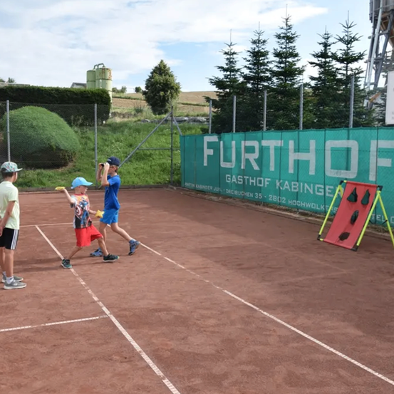 Drei Kinder spielen Tennis auf einem Tennisplatz, eines von ihnen hält einen Tennisschläger und ein anderes einen Tennisball.