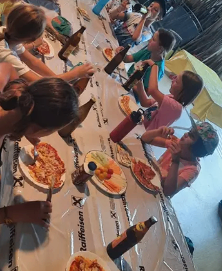 Eine Gruppe von Menschen sitzt an einem langen Tisch und isst Pizza und trinkt Bier.