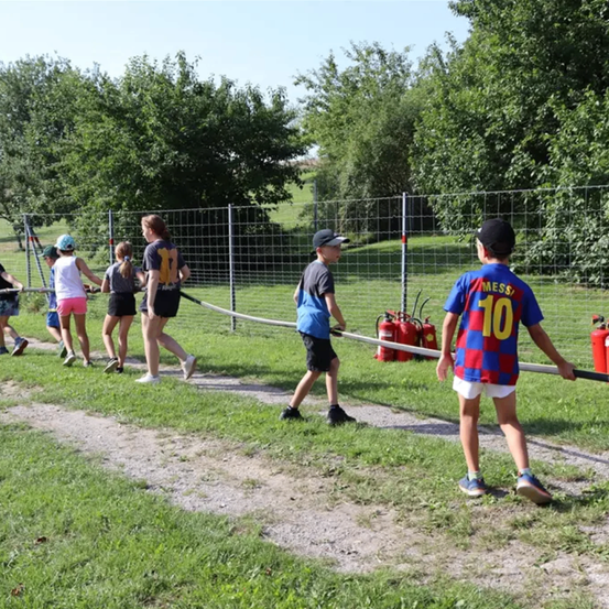 Eine Gruppe von Kindern in einem Park, die ein Seil ziehen, das an Feuerlöschern befestigt ist.