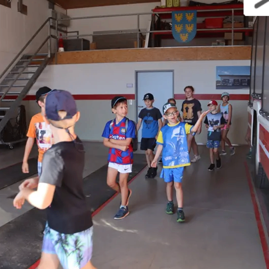 Mehrere Kinder in verschiedenen Shirts und Shorts gehen in einem Gebäude mit einem roten Feuerwehrauto an der Seite.