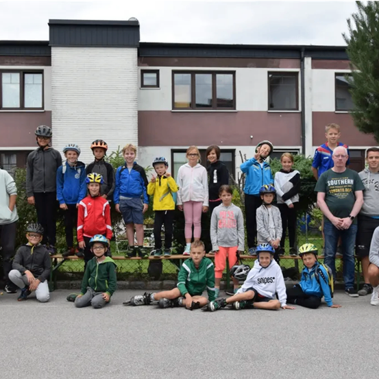 Gruppe von Kindern und Erwachsenen in Jacken und Helmen, die vor einem Gebäude für ein Foto posieren.