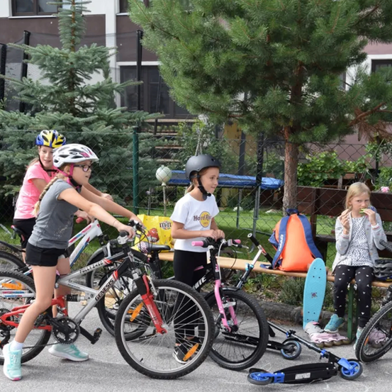 Fünf Mädchen stehen mit ihren Fahrrädern und Helmen. Ein Mädchen sitzt auf einer Bank und isst ein Sandwich.