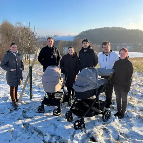 Eine Gruppe von Menschen steht im Schnee mit drei Kinderwagen, eine junge Frau hält einen Stock.