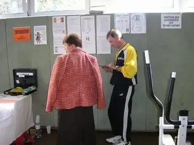 Ein Mann und eine Frau stehen vor einer Pinnwand, der Mann schaut auf sein Handy, während die Frau ihn ansieht.