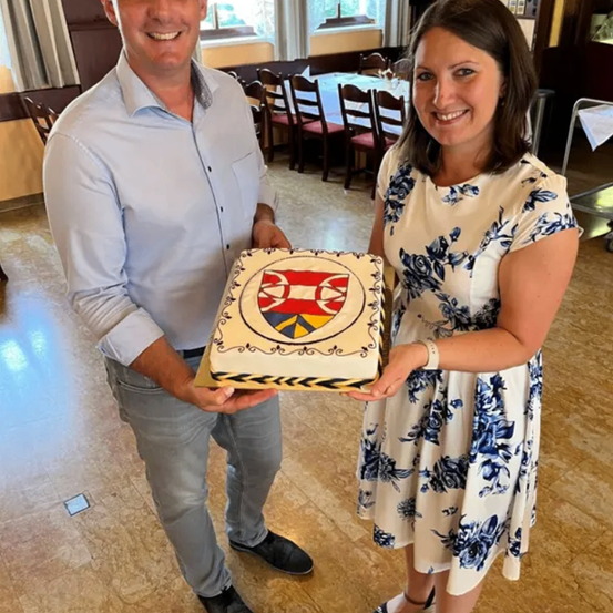 Ein Mann und eine Frau halten einen Kuchen mit einem Wappendesign in einem Esszimmer.