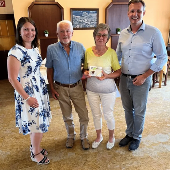 Vier Menschen stehen in einem Raum. Eine Frau hält ein Zertifikat. Sie alle lächeln.