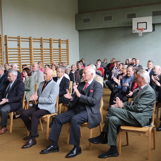 Eine große Gruppe älterer Menschen klatscht in einem Saal.