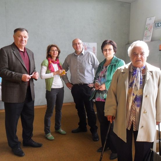 Fünf Menschen stehen in einem Raum, drei Frauen und zwei Männer, alle lächeln und posieren für ein Foto.