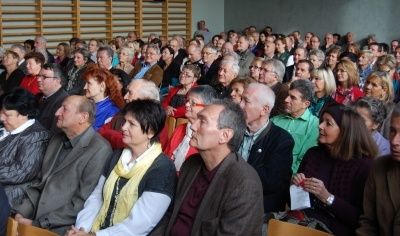 Ein großes Publikum sitzt in einem Konferenzsaal in Stühlen, trägt verschiedene Kleidungsstücke und einige Brillen und schaut nach vorne.