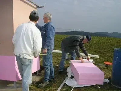 Vier Männer arbeiten auf einer Baustelle. Drei Männer stehen um eine pinke Struktur herum und ein Mann arbeitet auf einer pinken Struktur auf dem Boden.
