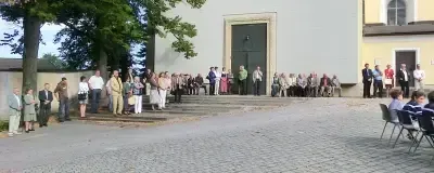 Eine Gruppe von Menschen steht auf den Stufen eines Gebäudes und schaut auf eine große Linde.