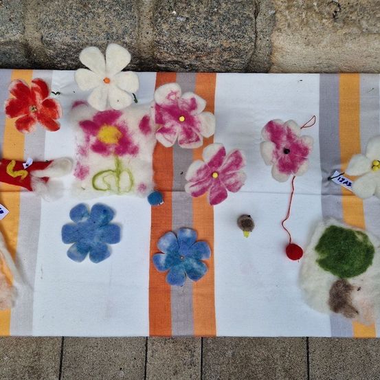 Ein farbenfroher Teppich mit verschiedenen Wollblumen in unterschiedlichen Farben und Größen, auf einer Steinoberfläche platziert.