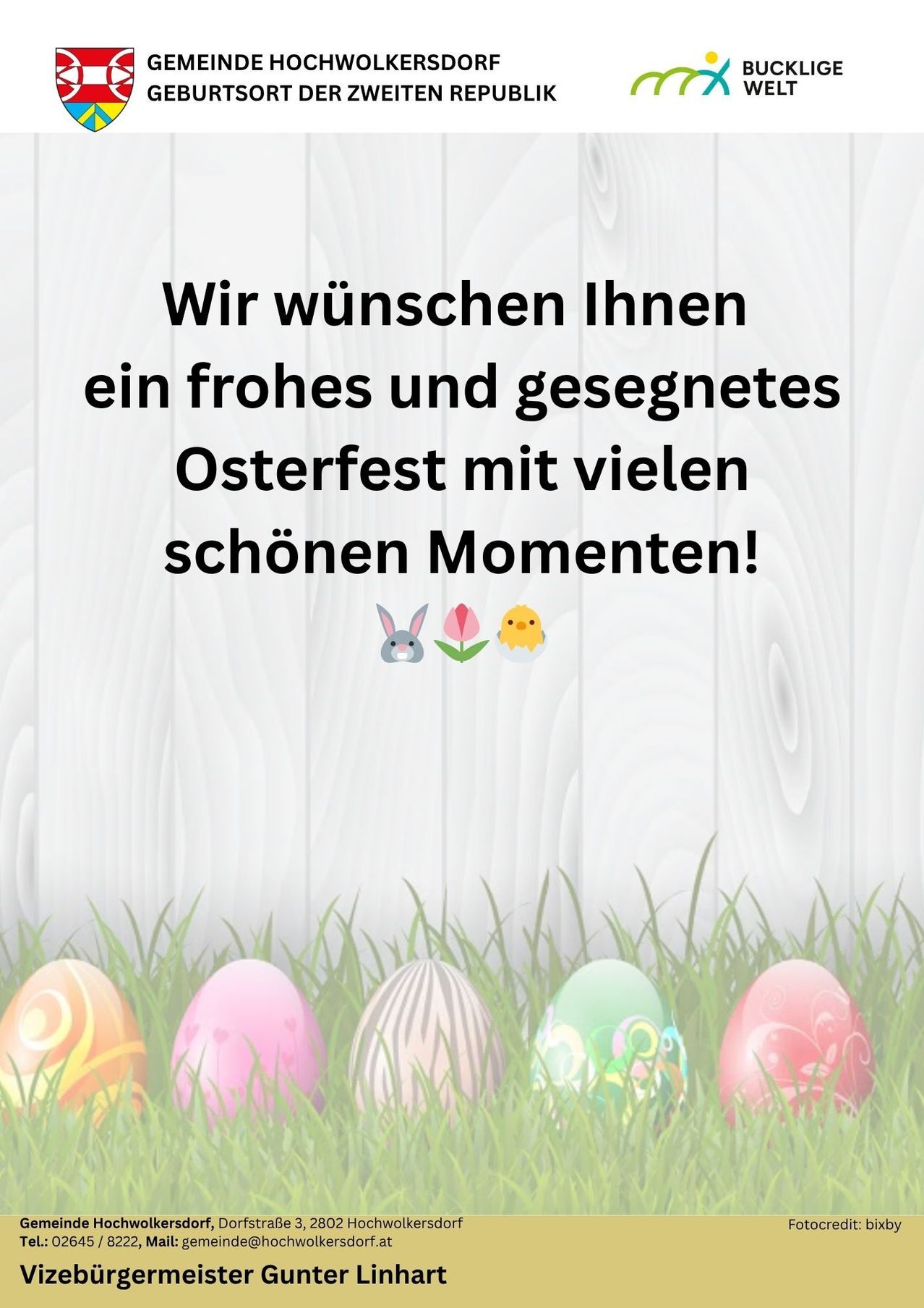 A white wooden background with Easter eggs and animals. The text reads, 'We wish you a happy and blessed Easter festival with many beautiful moments!' There are emojis of a rabbit, a chick, and flowers.