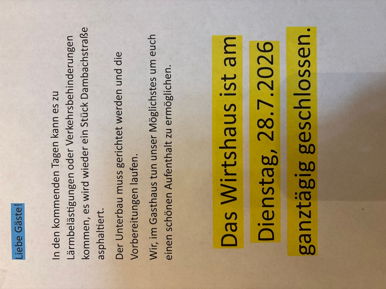 Ein gelbes Schild auf weißem Hintergrund zeigt den Text 'Das Wirtshaus ist am 28.7.2026 geschlossen' in schwarzer Schrift. Das Schild enthält auch Daten und eine Schließungserklärung.