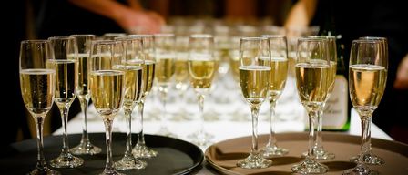 Mehrere Flutengläser mit Champagner stehen auf Tabletts auf einem Tisch, mit einer Person im Hintergrund.