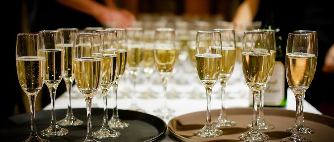 Mehrere Flutengläser mit Champagner stehen auf Tabletts auf einem Tisch, mit einer Person im Hintergrund.