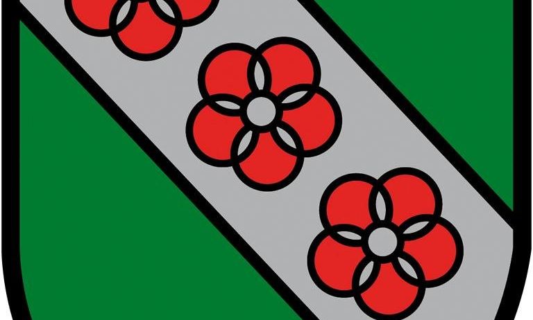 Ein grüner Schild mit einem weißen Band hat drei rote Blumen mit weißen Zentren darauf.