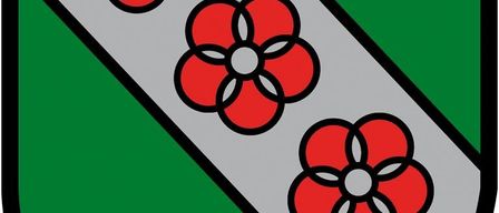 Ein grüner Schild mit einem weißen Band, das drei rote Blumen mit weißen Zentren hält. Der Schild hat einen schwarzen Rand.